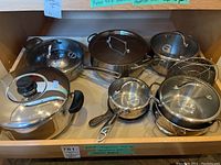 Overview of all cookware items on shelf including stainless steel and nonstick pieces plus steamer baskets