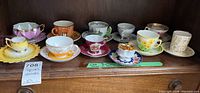 Wide view of assorted teacups with matching saucers on wooden cabinet surface