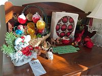 Wide shot of basket filled with assorted vintage Christmas ornaments including glass balls, cardinal birds, and animal decorations alongside box of additional ornaments and decorative mouse figure
