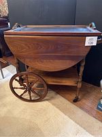 Closed wooden bar cart with drop-leaf side wings folded down and large wooden spoked wheels visible on one side.