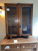 Front view of oak cabinet showing double leaded glass doors, central stile, tassel key and bracket feet