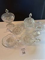 Group photo of six crystal serving pieces including 2 lidded dishes, 3 handled divided dishes, and 1 pedestal dish with scalloped edges.
