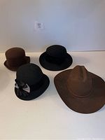 Four felt hats including a large brown cowboy hat and three women's felt hats in black and brown.