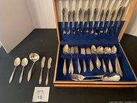 Top and inside view of the wood storage box with rows of knives, forks, spoons arranged inside, and several utensils laid out to the left on a black surface.