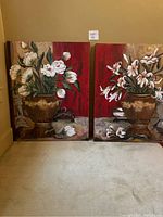 Two floral canvas paintings side by side showing brown vases with white flowers against a red and beige background.