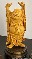 Front view of Laughing Happy Buddha figurine showing facial detail, raised arms, necklace, robe folds, and wooden base.