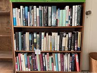 Full view of three shelves densely packed with hardbound and paperback books, showing titles and spines clearly.