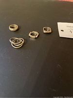 Four silver rings arranged on a surface, showing different styles and shapes.