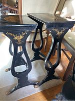 Two black lacquered Chinese nesting tables shown nested together, highlighting curved legs with floral gold detailing and claw feet.