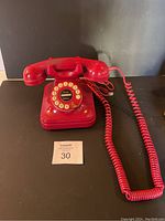 Front view of red push button telephone with handset and coiled cord laid out on black surface.