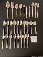 Photo showing full assortment of flatware and serving pieces arranged on a black background, including spoons, forks, and serving utensils.