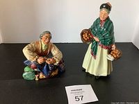 Front view of The Orange Lady and The Tailor porcelain figurines on black background