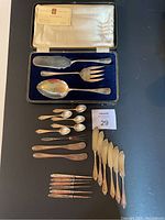Open case showing fish server spatula, serving fork and serving spoon atop blue velvet lining, plus assorted utensils below