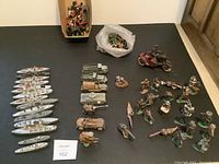 Top-down photo showing all items spread out on black surface including navy ships, vehicles, soldiers, and plastic mounted police figures.
