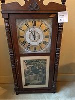 Front view of the wooden clock showing Roman numeral dial and lower art panel.