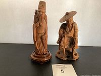 Front view of two Asian wood carved figures, standing and seated, showing details and damage.