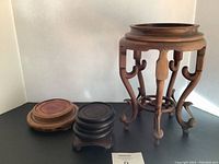 Photo showing a tall wooden stand with carved legs alongside four smaller round wooden stands on a black surface.