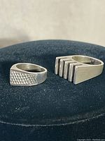 Two vintage sterling silver rings placed on a black surface, showing front views with distinct geometric designs.