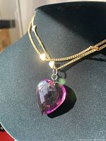 Closeup photo of the necklace draped on a black bust showing the gold-tone double chain with heart accents and the purple glass heart pendant.