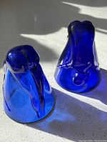 Two cobalt blue glass human form figurines shown from front angle on light surface, highlights transparency and shape details.
