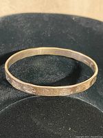 Full view of oval sterling silver Mexican bracelet with carved and stamped decorative pattern on black background.