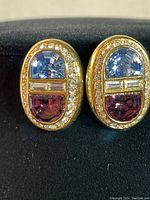 Front view detail of both earrings showing outer clear rhinestone border, blue-violet top glass stones, purple bottom glass stones, and rectangular baguette rhinestones in the center