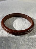 Photo of the full round vintage brown Bakelite cuff bracelet lying flat on a pale cloth surface, showing smooth, rounded edges and polished surface.