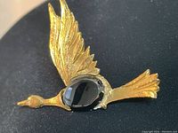 Close up photo of vintage goose brooch showing gold-tone textured wings, body with oval black stone, and rhinestone eye.
