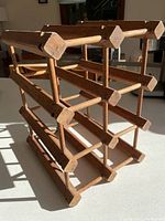 Front angled view of the vintage teak MCM Danish wine rack showing three horizontal shelf rows designed to hold 6 to 8 bottles.