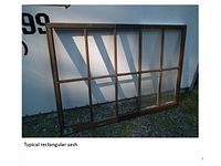 Typical rectangular wooden sash frame with multiple glazing panes leaning against a white surface outdoors