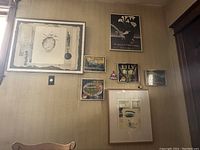 Wide view photo showing six framed art pieces arranged on a wall, including prints and advertising labels