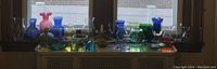 Long shot showing the full assortment of colored glass pieces displayed on a window ledge with various colors including blue, pink, green, and clear glass items.