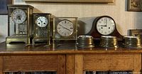 Photo shows the four clocks and three brass Bulova weather station instruments arranged on a wooden surface.