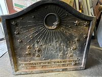 Front view of cast iron fireback showing crescent moon face, sun rays, stars and inscription.