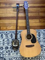 Photo showing acoustic guitar and Sanxian side by side on a patterned rug, highlighting the natural wood finish of the guitar and the snakeskin resonator of the Sanxian.