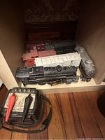 Photo showing the entire set including black steam locomotive, coal tender, several boxcars, tanker car, and wired controller on wooden floor shelf.