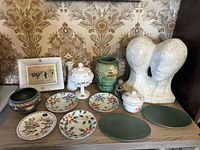 Wide view of all porcelain, pottery, glass, and sculpture items arranged on surface with wallpaper background.