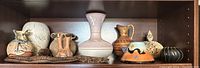 Shelf with multiple Southwestern American pottery and ceramic vessels including pitchers, vases, and small pots with traditional painted designs.