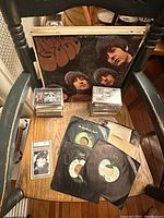 Photo showing Beatles 'Rubber Soul' vinyl LP and various Beatles 45 rpm singles and cassette tapes along with Ringo Starr card.