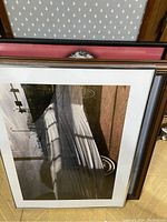 Framed photographic print showing a covered boat or similar object reflected on water. Wooden frame with white mat.
