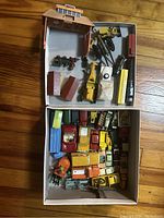 Two open cardboard boxes showing approximately 40 diecast vehicles and a small cardboard garage diorama