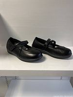 Side view of pair of black Orthofeet women's orthopedic comfort shoes with Velcro straps on platform shelf.