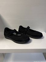 Pair of Orthofeet black ladies shoes in Mary Jane style shown at a side angle to display shape and adjustable strap.