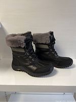 Side view of black UGG Adirondack II women's boots with gray shearling collar, showing lace-up front and Gore-Tex label.