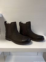Front and side angled view of brown UGG men's ankle boots showing leather toe and suede body.