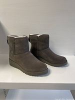 Side view of the pair of taupe women's UGG boots showing the soft suede texture, round toe, and rubber sole.