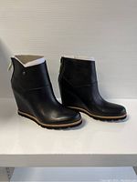 Front-side angled view of black leather wedge boots showing smooth finish and wedge heel design.