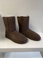 Front angled view showing brown UGG Classic Short boots with original paper stuffing inside.
