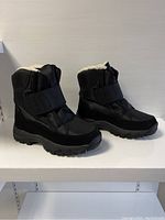 Side angled view of black winter boots showing overall shape, sole design and velcro straps.