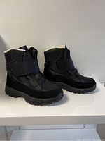 Front-side view of pair of black unisex winter boots placed on white surface against neutral background showing overall design and materials.